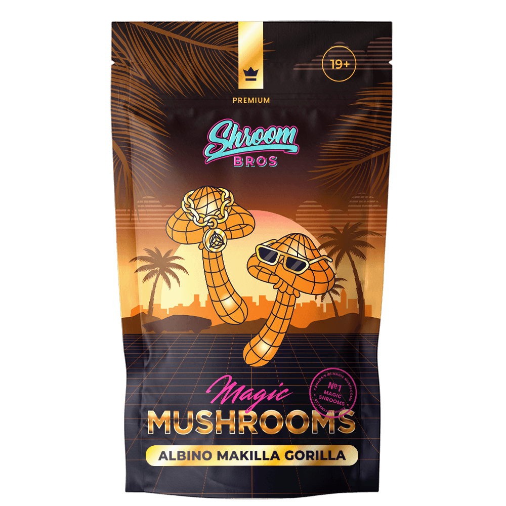 Shroom Bros Premium Albino Makilla Gorilla Magic Mushrooms packaging featuring stylized mushroom characters with gold chains and sunglasses against a tropical sunset cityscape backdrop.